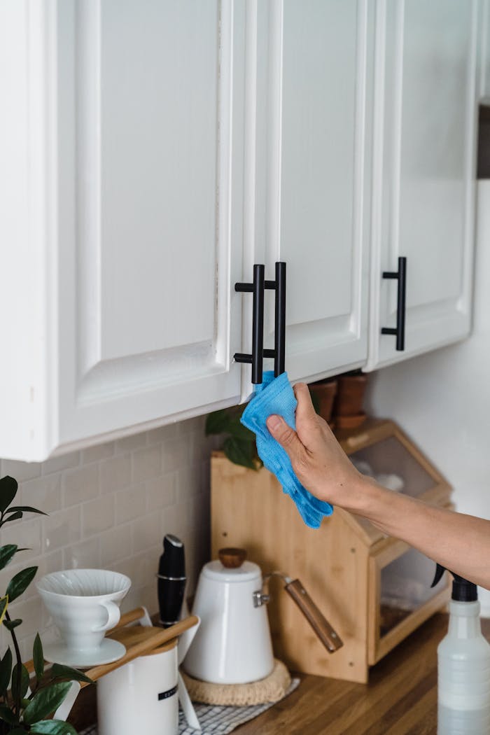 A person using a blue cloth to clean white kitchen cabinets with black handles.